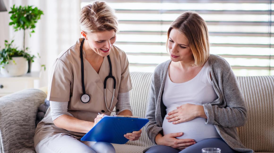 Położna podczas wizyty domowej u pacjentki w zaawansowanej ciąży. Omawiają wyniki badań.