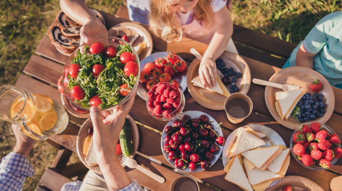 Widok z góry na stoł, na którym są na talerzach pomidory, maliny, czereśnie, truskawki, kanapki z serem oraz roszponka.