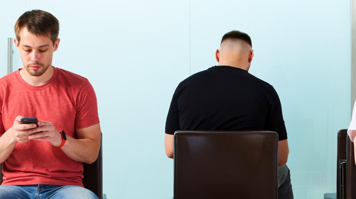 Trzy osoby siedzą na krzesłach w poczekalni w przychodni. Patrzą w telefony.