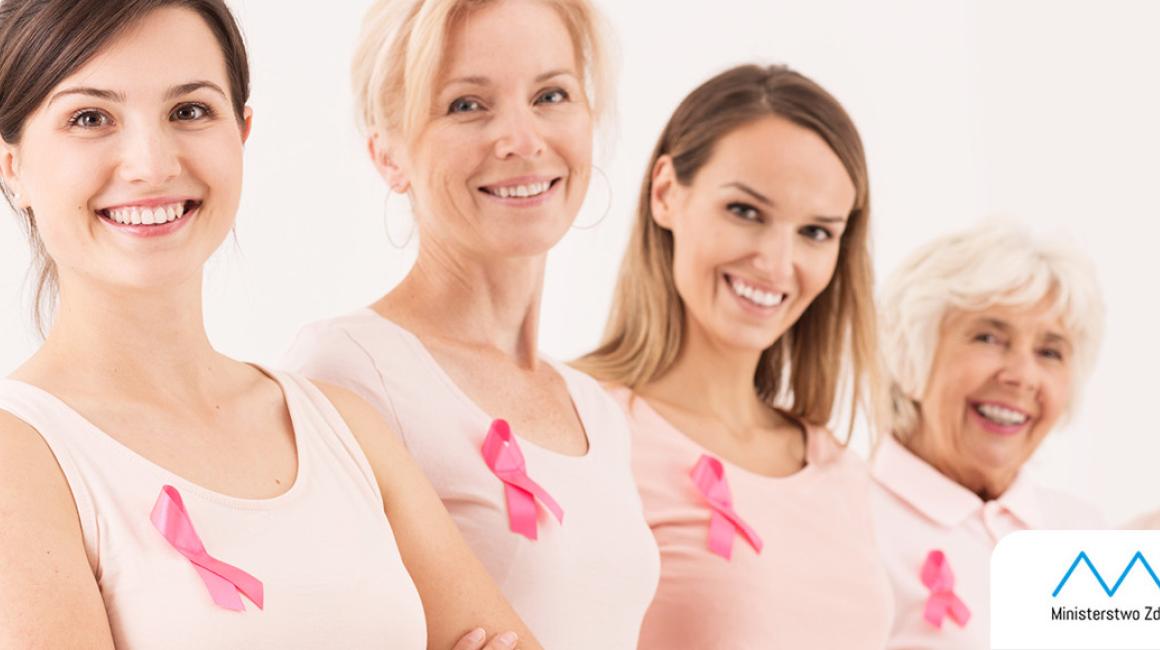 Uśmiechnięte kobiety stojące w rzędzie. Do piersi przypiete mają wstążeczki - symbol walki z rakiem piersi.