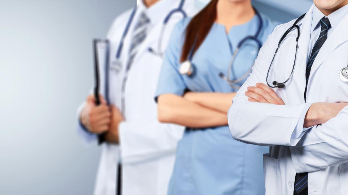 Trójka lekarzy z stetoskopami na szyi stoi w rzędzie. Zbliżenie na ich ręce założone na siebie.