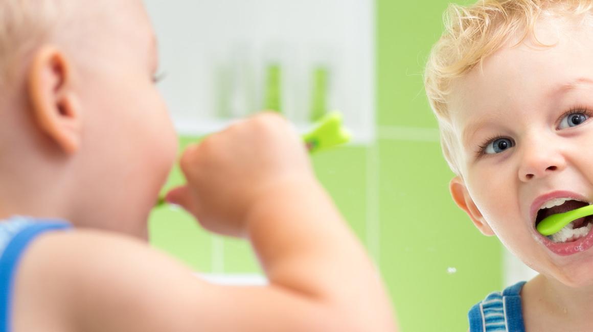 Mały chłopiec myjący zęby w łazience. Odbicie w lustrze.