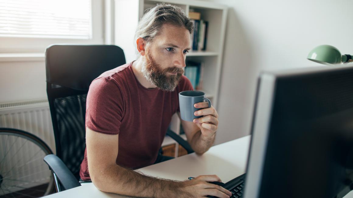 Brodaty mężczyzna z kubkiem przed laptopem