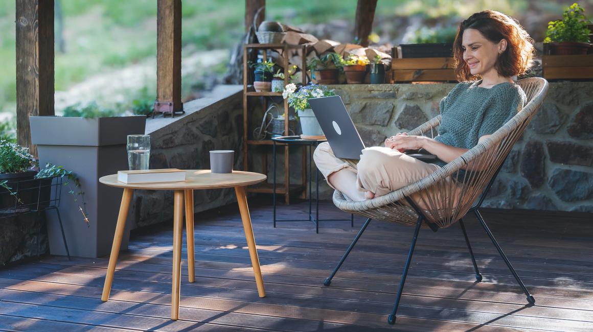 Kobieta na werandzie w wiklinowym fotelu z laptopem