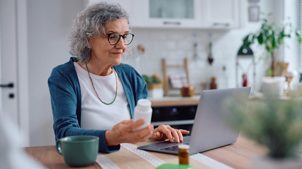 starsza pani przy komputerze z opakowaniem leku w  ręku 