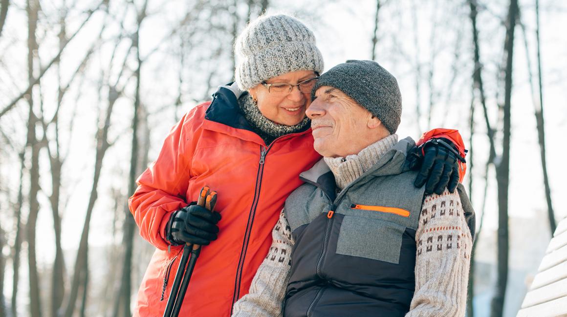 Starsza para na zimowym spacerze, on siedzi, ona go obejmuje