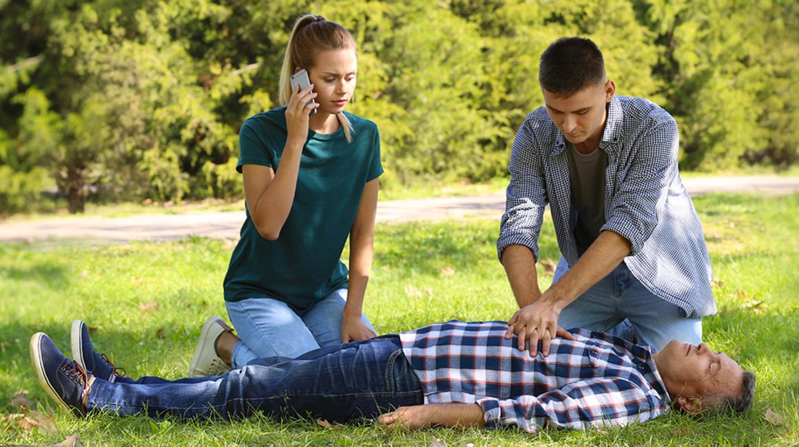park, poszkodowany leży, dziewczyna dzwoni, chłopak robi masaż serca