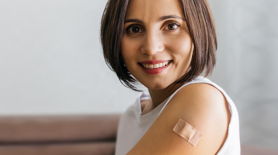 uśmiechnięta kobieta z plastrem na lewym ramieniu