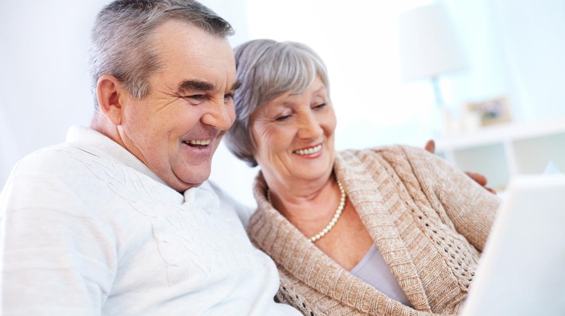 Starsza para z uśmiechem patrzy na ekran laptopa