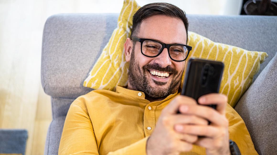 Mężczyzna w żółtej koszuli leży na kanapie z telefonem