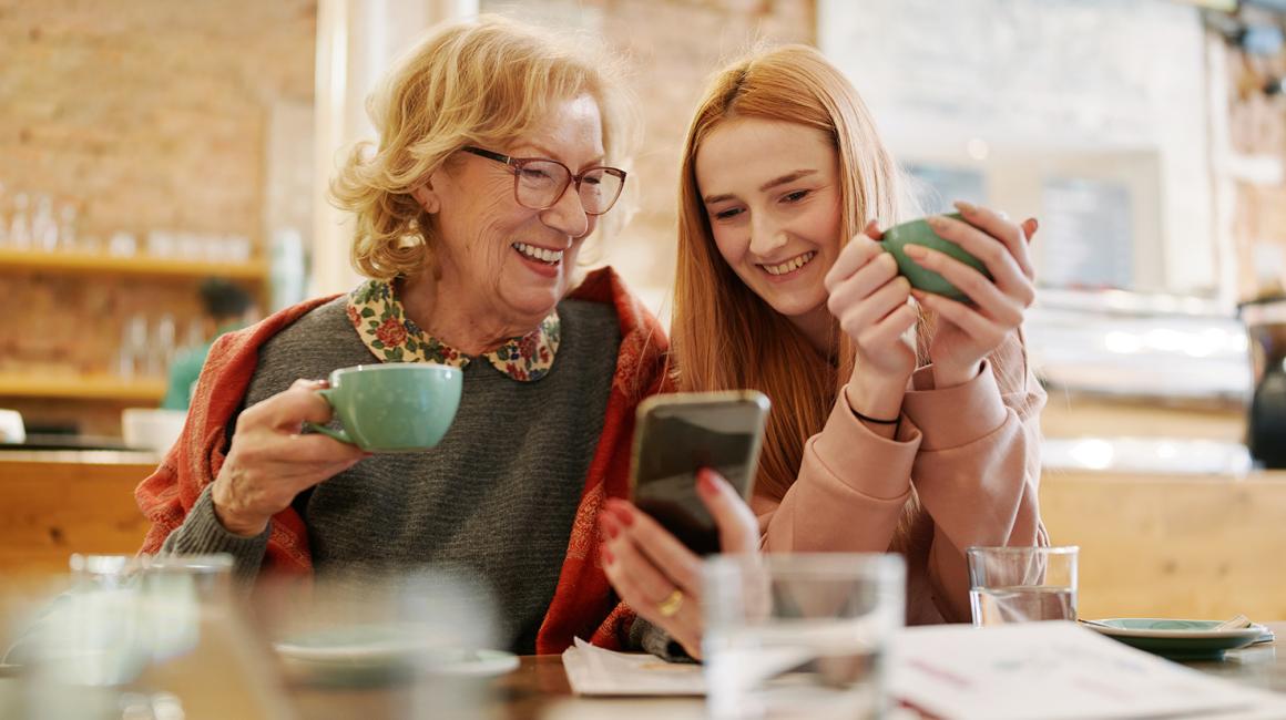 Babcia i wnuczka patrzą na telefon komórkowy, pijąc herbatę w kuchni