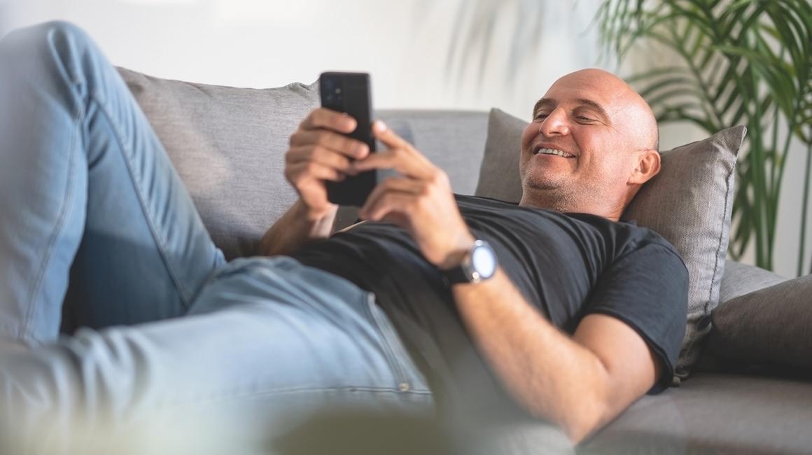 łysy uśmiechnięty facet leży na kanapie z komórką