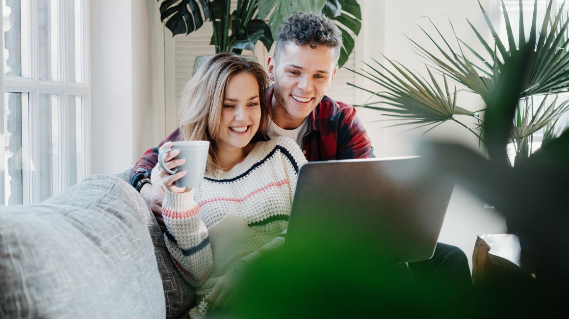 uśmiechnięta para młodych na kanapie przed laptopem