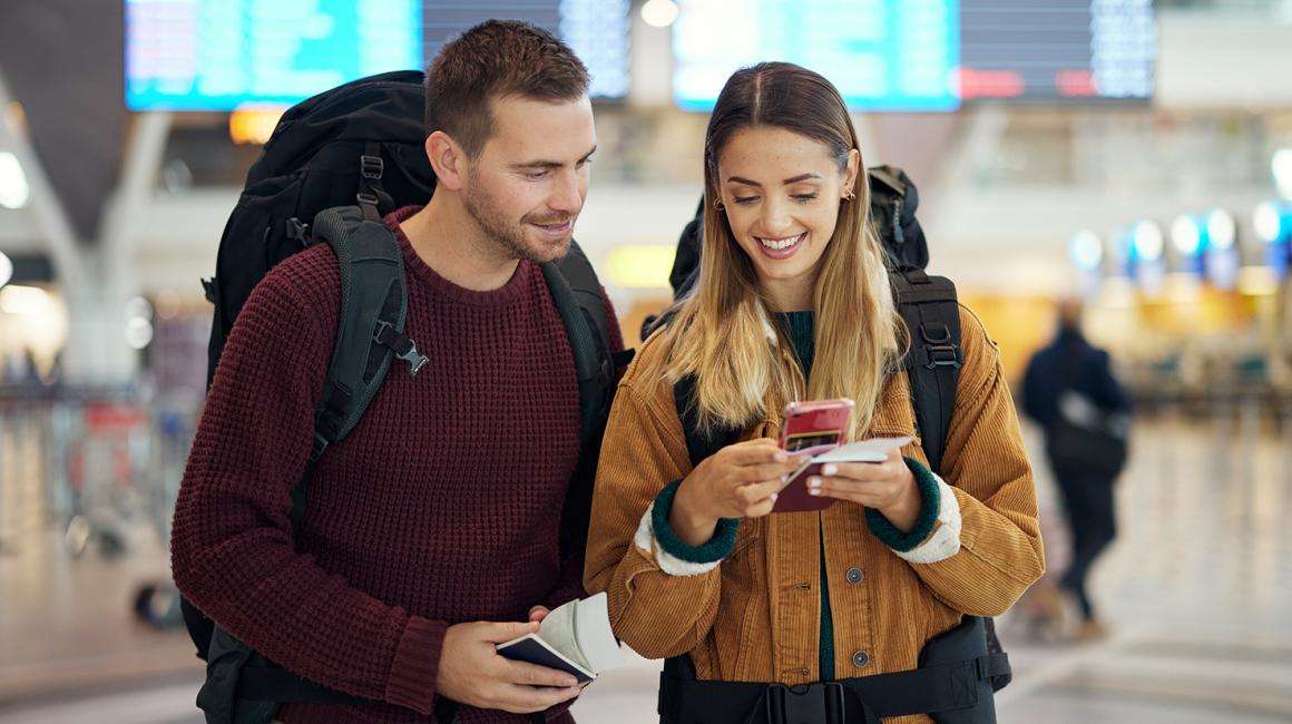 mlodzi ludzie na lotnisku z plecakami patrza na telefon