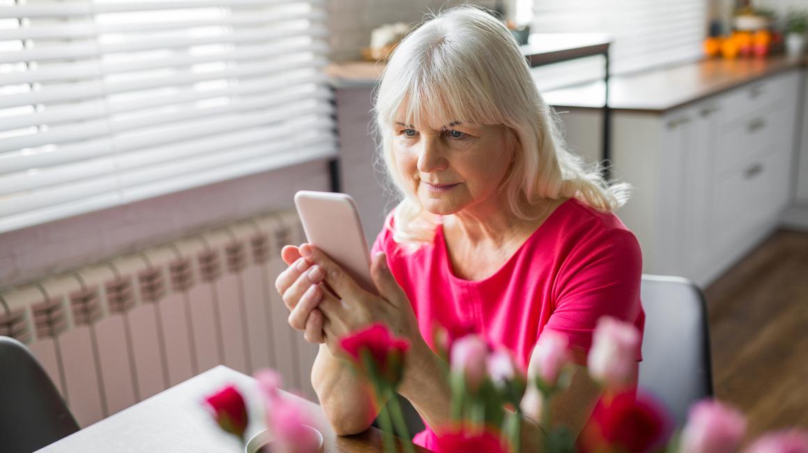 Starsza pani w czerwonej bluzce, z komórką, przed nią tulipany