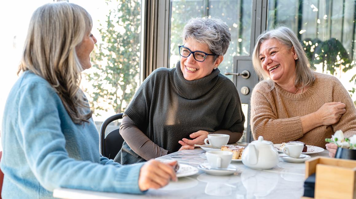 trzy kobiety w średnim wieku przy wspólnym stole, jedna patrzy na komórkę