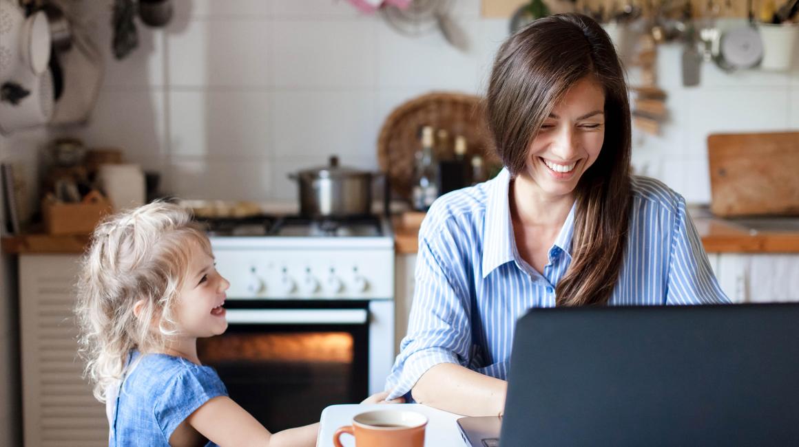Uśmiechnięta matka przed laptopem, obok smieje się kilkuletnia córka