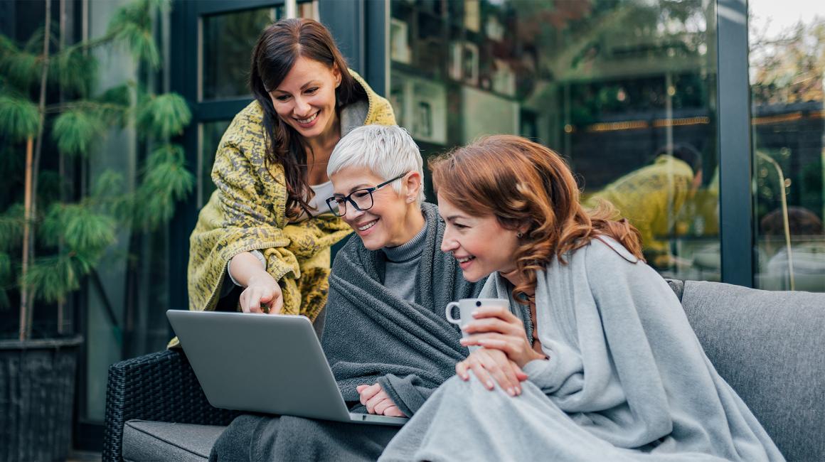 trzy przyjaciółki, jedna pokazuje coś dwóm pozostałym na laptopie