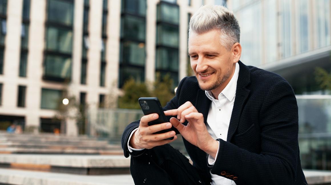 Mężczyzna w garniturze z telefonem siedzi przed biurowcem