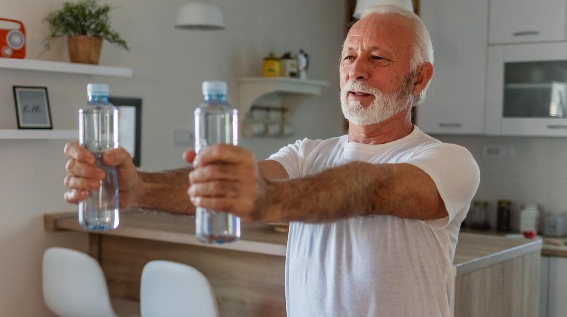 starszy pan ćwiczy w domu z małymi butelkami wody