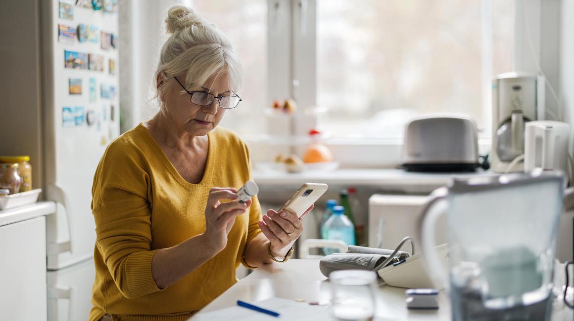 starsza pani w kuchni z pojemnikiem leków i komórką w rękach