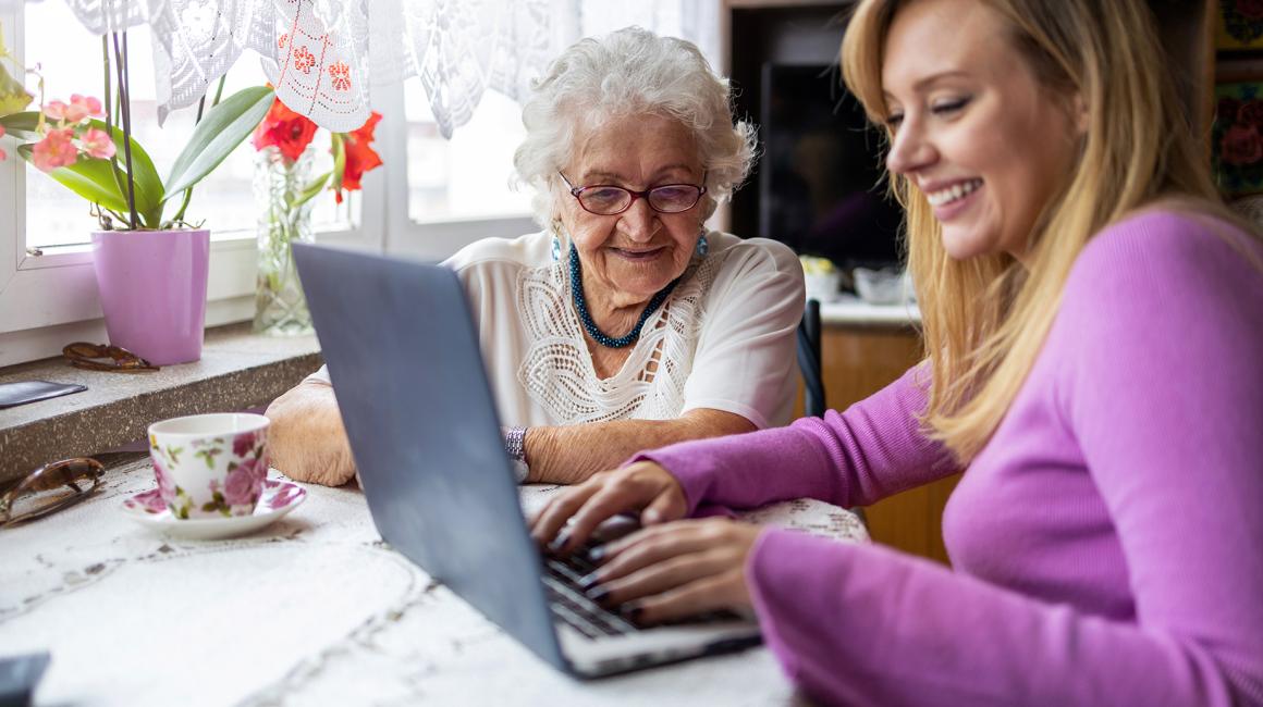 Babcia i wnuczka siedzą przy stole z herbatą i komputerem