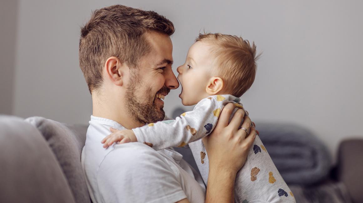 Tata z małym dzieckiem, trzyma je w ramionach i patrzą na siebie