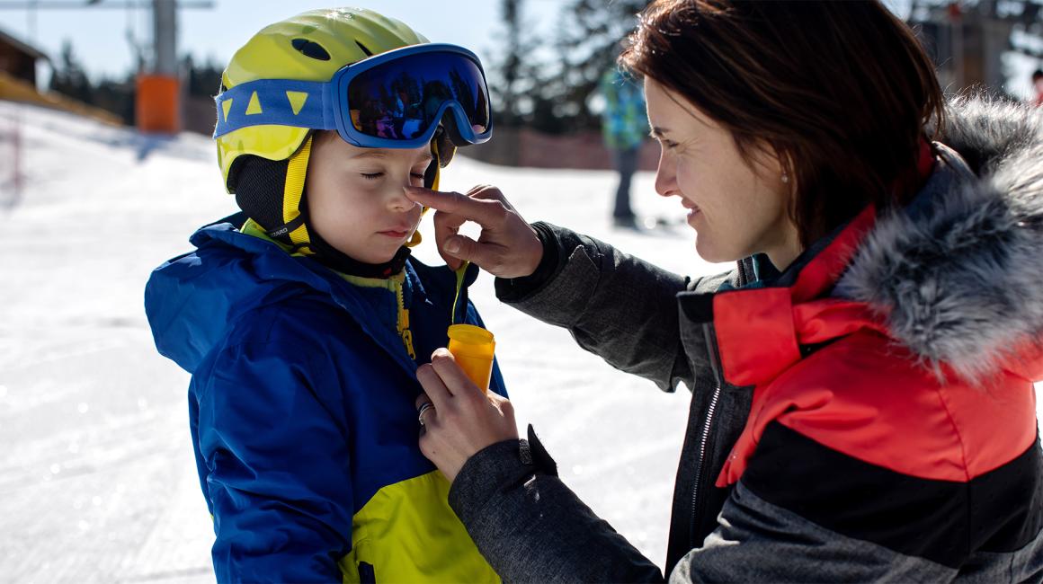 mama smaruje dziecku nos, oboje na stoku narciarskim