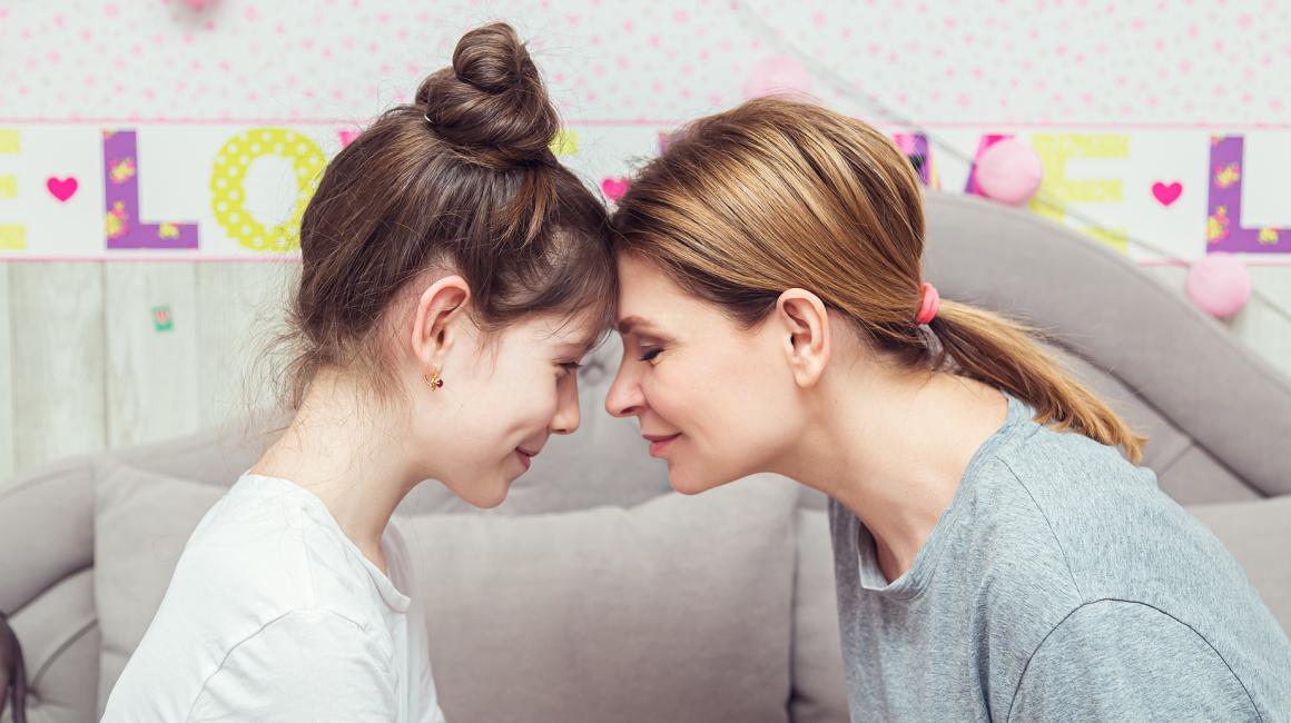 Matka i córka czule dotykają się czolami, nastolatka w koku, matka z rozpuszczonymi