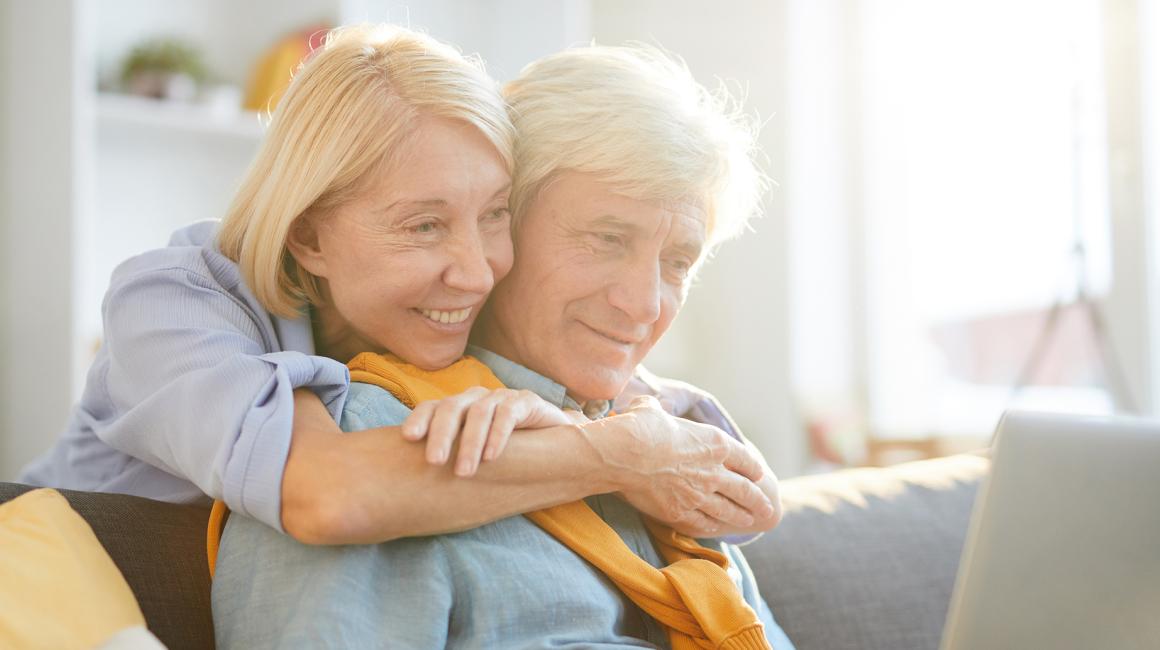 50letnia pani obejmuje za szyję męza, on patrz w laptop