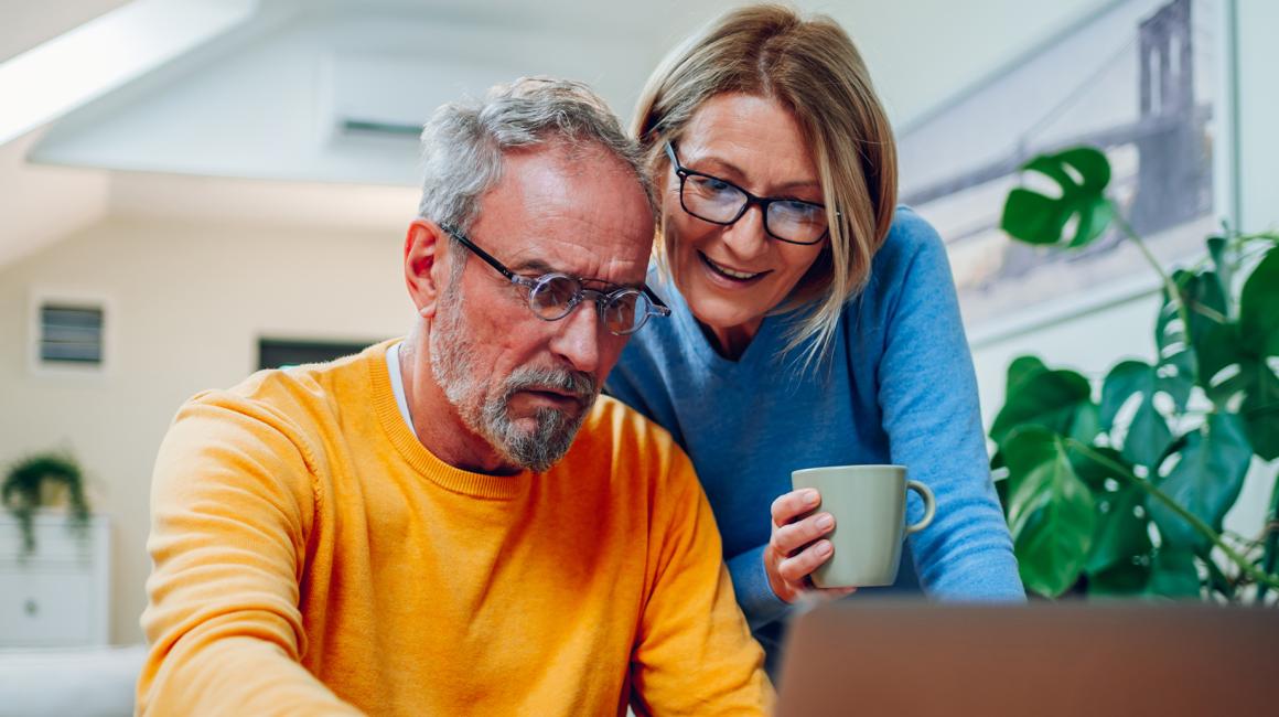 Kobieta z kubkiem kawy pokazuje coś na ekranie kompa mężczyźnie