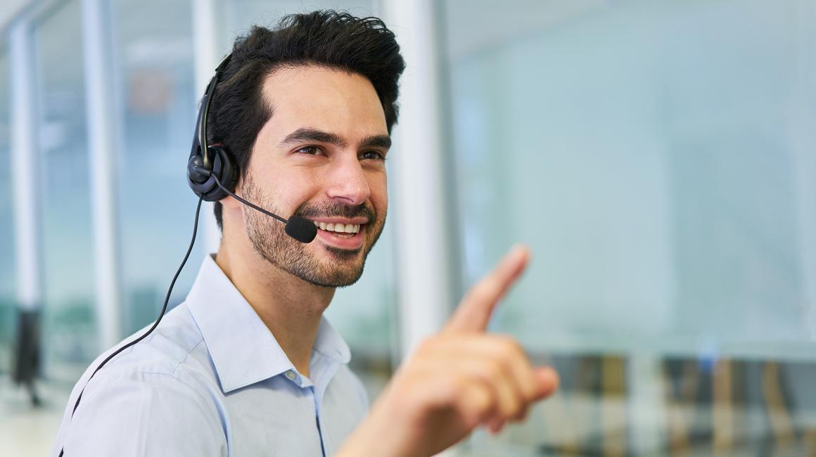 Mężczyzna w słuchawkach  infolinii palcem wskazującym prawej ręki na coś pokazuje
