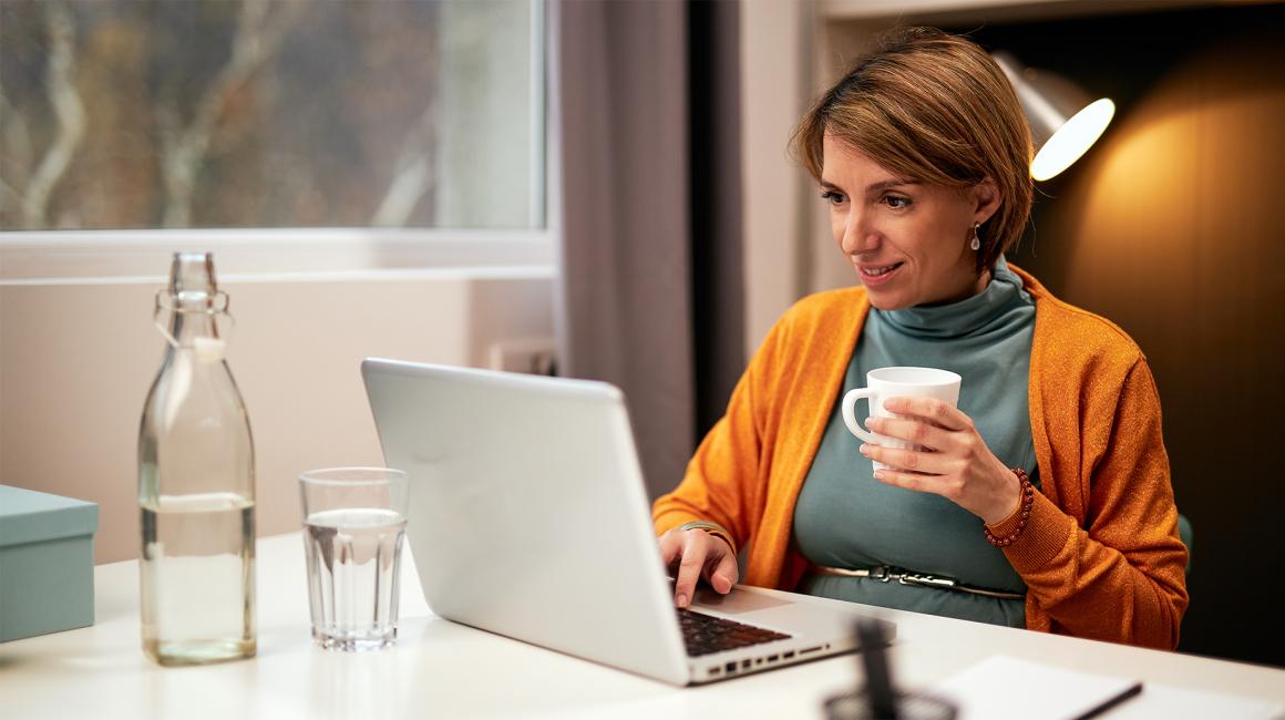 kobieta w sweterku na golfie przy stole z laptopem i herbatą