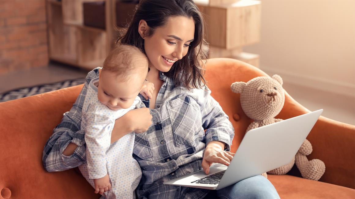 Matka z rocznym dzieckiem na kanapie, laptop ma na kolanach