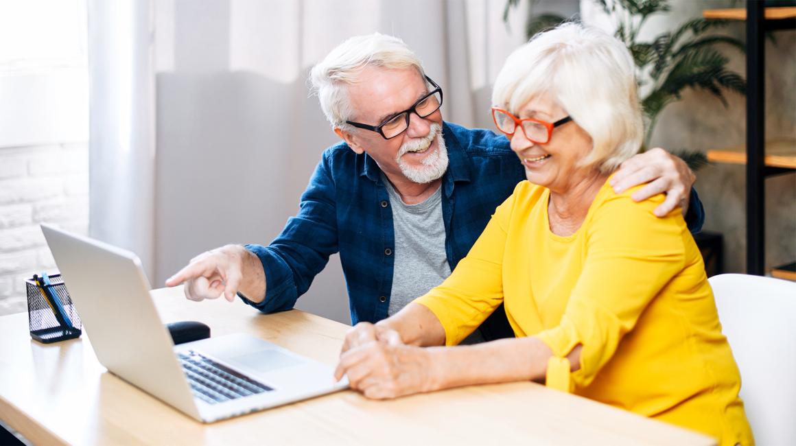 para starszych osób, Pan pokazuje z uśmiechem na treść na laptopie pani