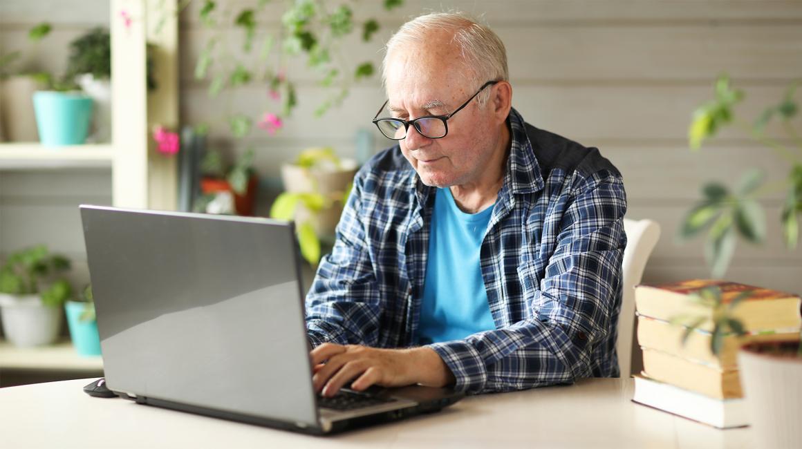 Starszy, siwy pan we flanelowej koszuli przed komputerem
