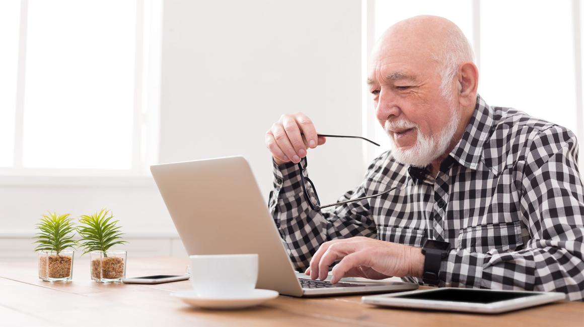 Starszy pan z brodą i okularami w ręku przed komputerem