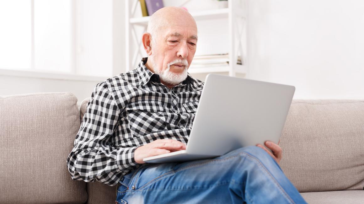 Starszy pan z broda z laptopem na kolanach na kanapie