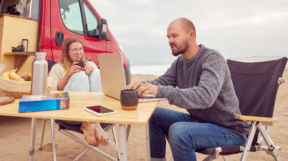 para przed kamperem, mężczyzna przy laptopie, w tle plaża