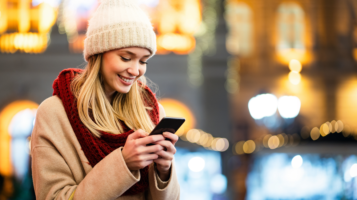 Kobieta z komórką, w czapce, w tle nocne miasto