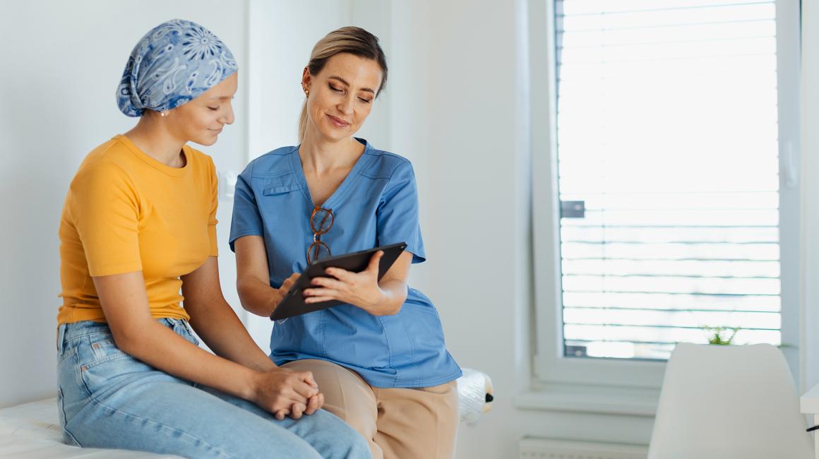 Pani w chustce rozmawia z lekarką,która coś jej pokazuje na tablecie
