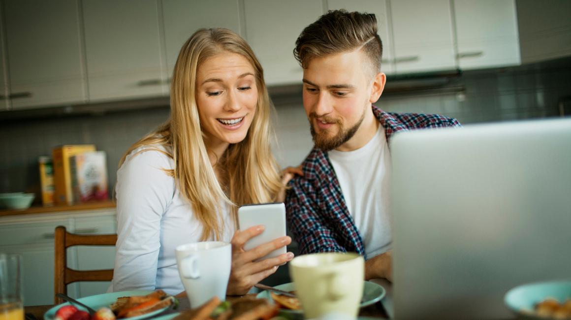 po sniadaniu w kuchni, cz\lopak przed laptopem patrzy na dziewczynę z komórką
