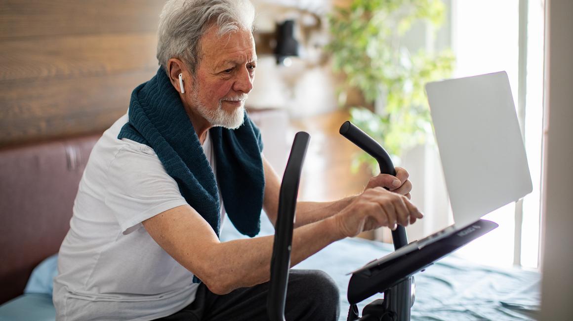 Starszy pan na orbitreku i z laptopem