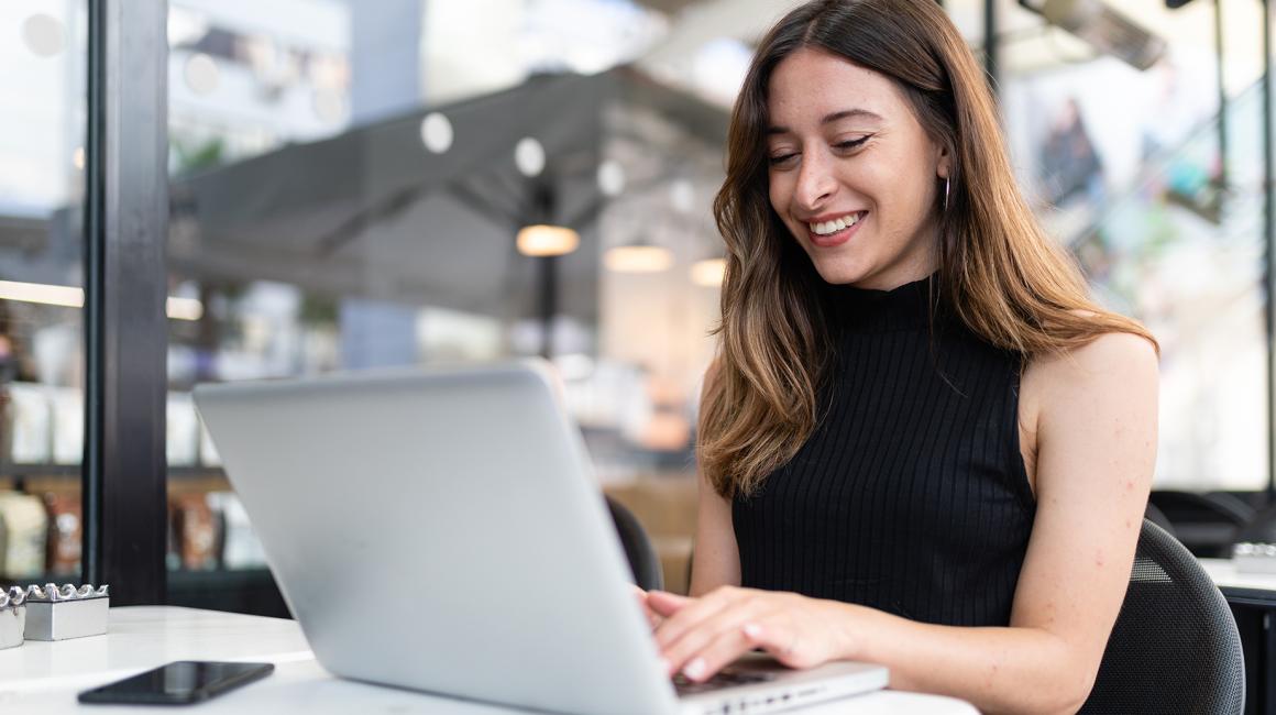 uśmiechnięta kobieta przed laptopem, ma długie włosy