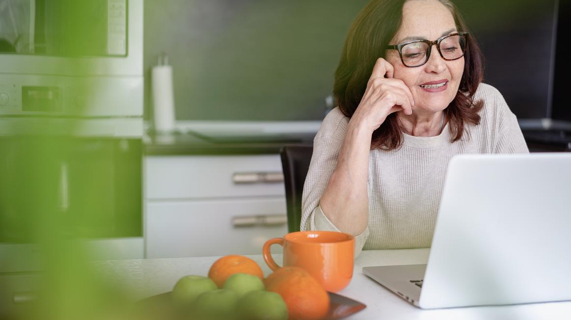 Kobieta ok 60ki przed laptopem, obok niej taca z pomarańczami