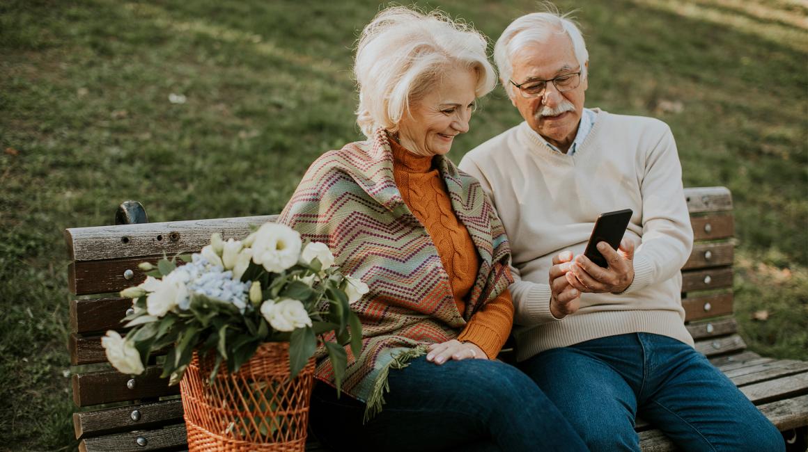 Starsza para na ławce, on pokazuje jej coś w telefonie