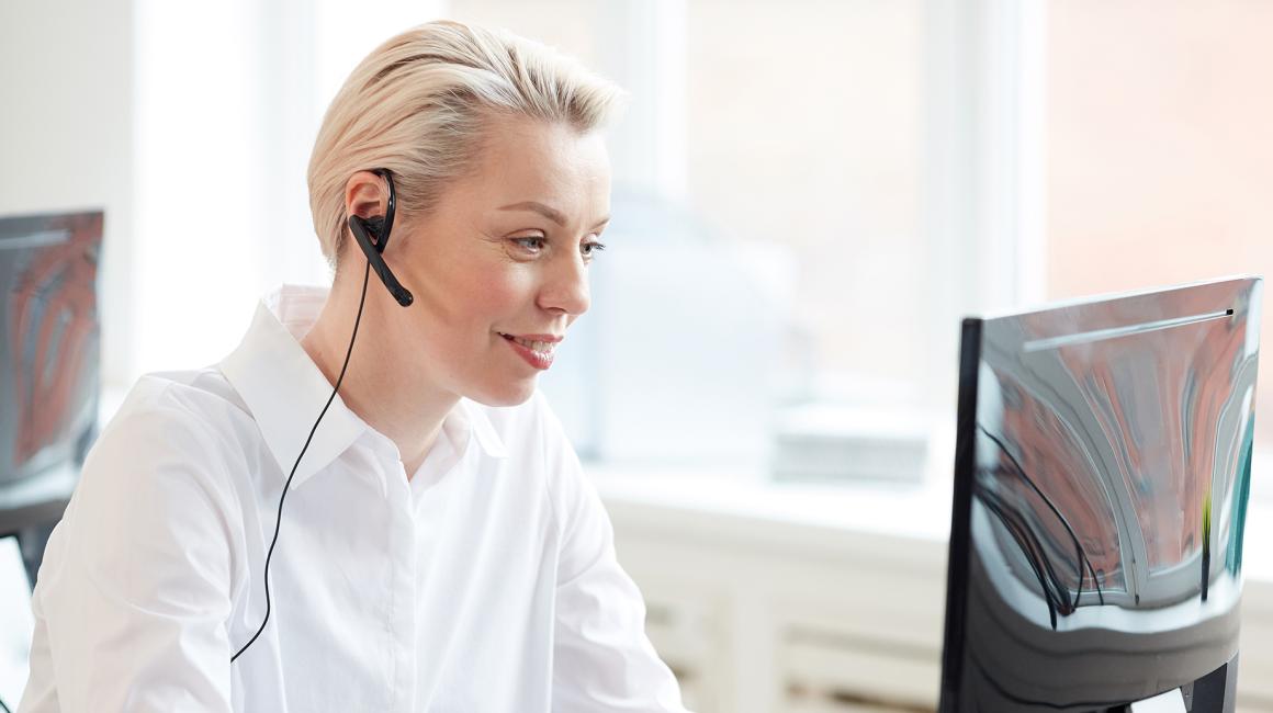 Pani w białej bluzce ze słuchawkami w uszach przed komputerem