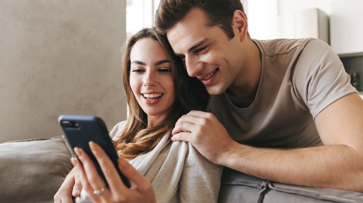 ona siedzi na kanapie i pokazuje mu coś na komorce, on pochyla się nad nią i zagląda jej przez ramię