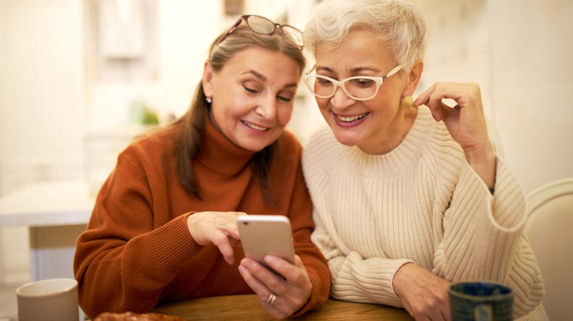Dwie panie ok. 60 lat, jedna pokazuje drugiej coś w komórce