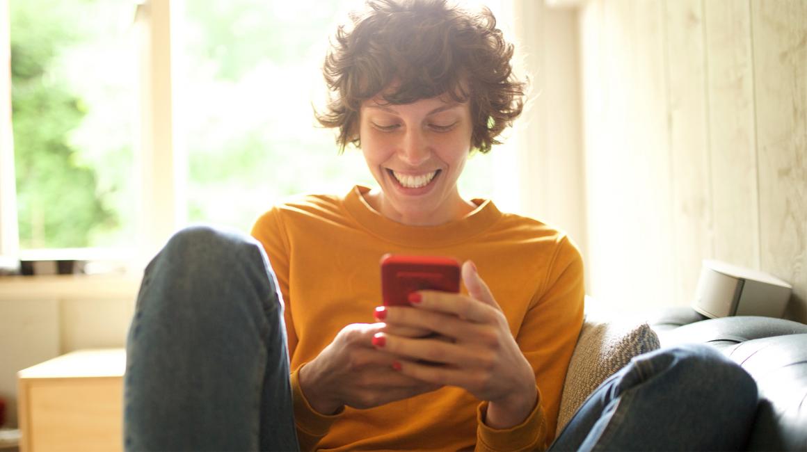 Roześmiana dziewczyna trzyma w ręku telefon i patrzy na ekran